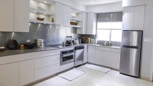 A modern kitchen with white cabinets, stainless steel appliances, and a tiled backsplash. - Stunning beachfront condo. Relax, Enjoy, Sunset, RumPoint, Pool & Heated Jacuzzi (Grand Cayman)
