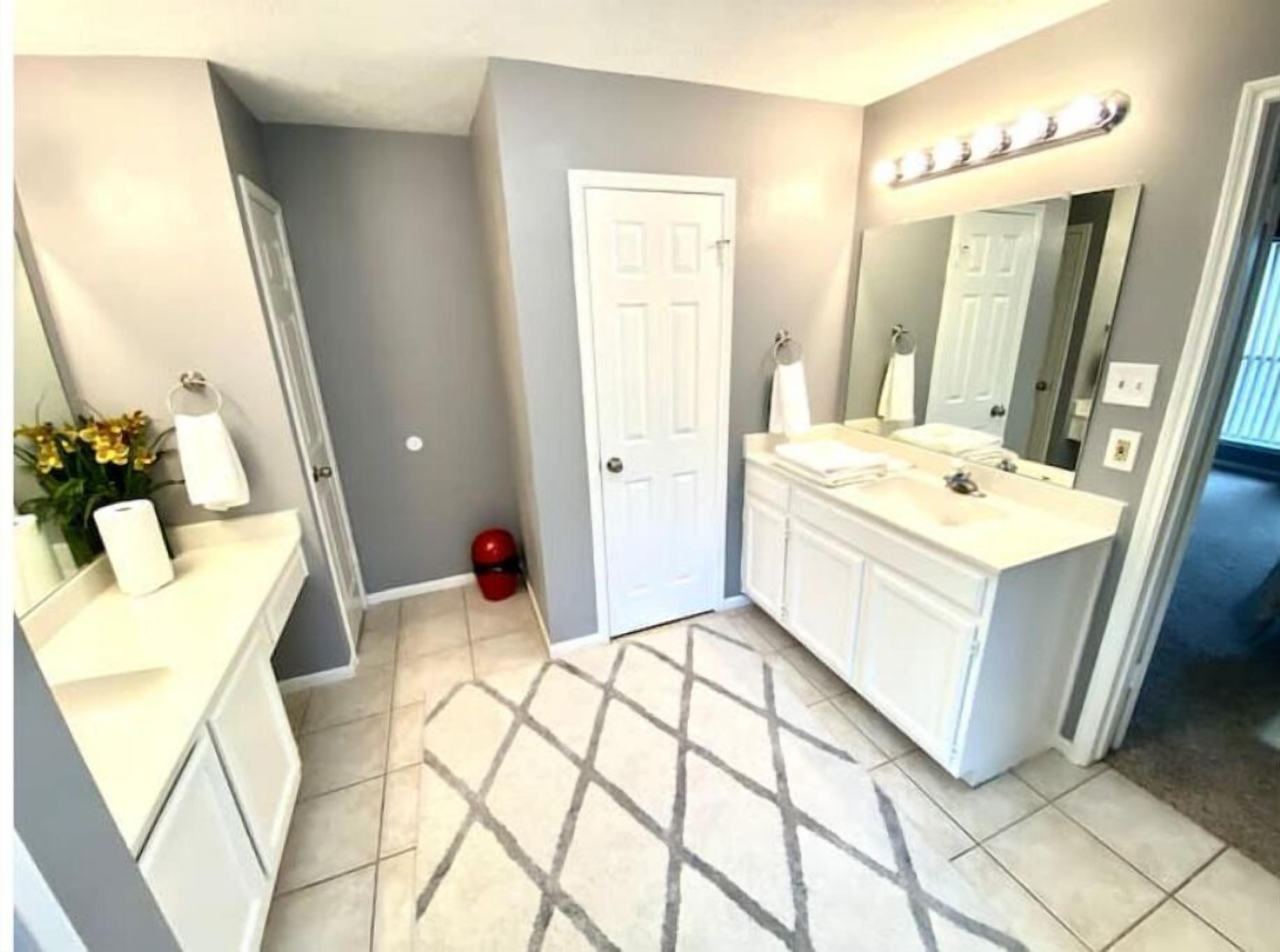 A bathroom with a vanity, a large mirror, and a lighted vanity area.