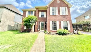 A two-story brick house with a front entrance, a small front yard, and a black metal fence. - Cozy Duplex Close to Hobby, Lagoon, NASA, Beaches! (Pasadena)