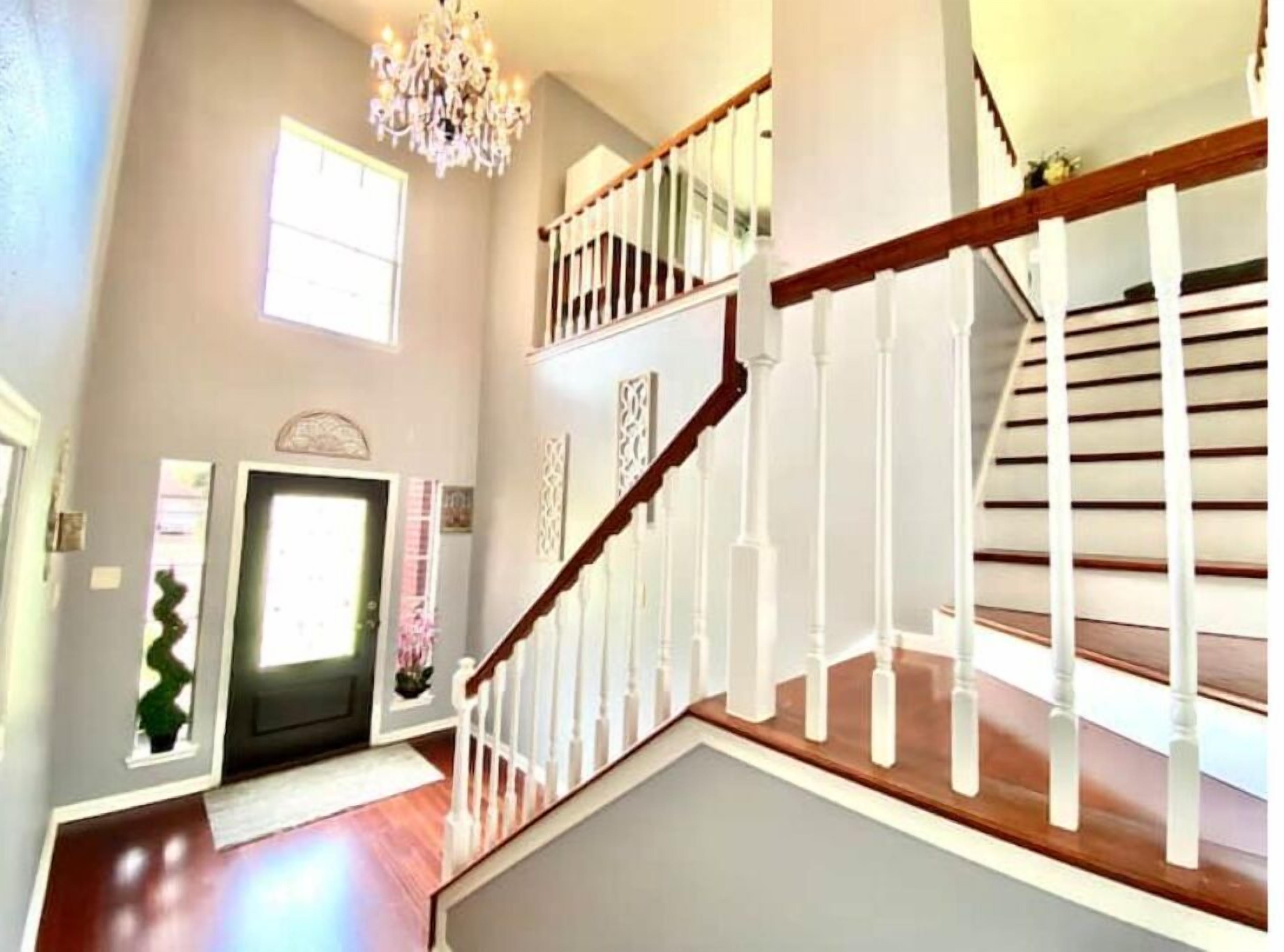 Un intérieur spacieux agrémenté d’un escalier en bois, d’un lustre et d’une porte donnant sur une autre pièce.