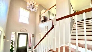 A spacious interior with a wooden staircase, a chandelier, and a door leading to another room. - Cozy Duplex Close to Hobby, Lagoon, NASA, Beaches! (Pasadena)