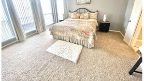 A bedroom with a large bed, a nightstand, a window with curtains, and a ceiling fan. - Cozy Duplex Close to Hobby, Lagoon, NASA, Beaches! (Pasadena)