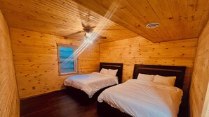 A cabin with two wooden bunk beds, a ceiling fan, and a window with blinds.