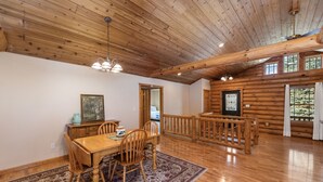 A spacious dining area with a wooden table and chairs, a patterned rug, and a wooden ceiling with exposed beams.
