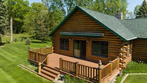A log cabin with a deck, surrounded by a well-maintained lawn and trees.