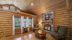 A log cabin interior with a fireplace, wooden furniture, and a stone accent wall.
