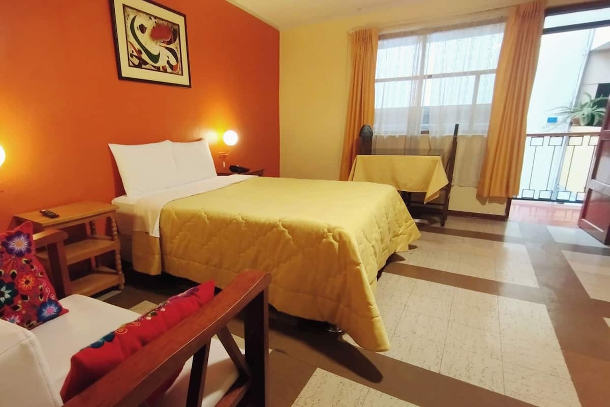 Ein Hotelzimmer mit Bett, Sessel, kleinem Tisch und einem Fenster mit Vorhängen.