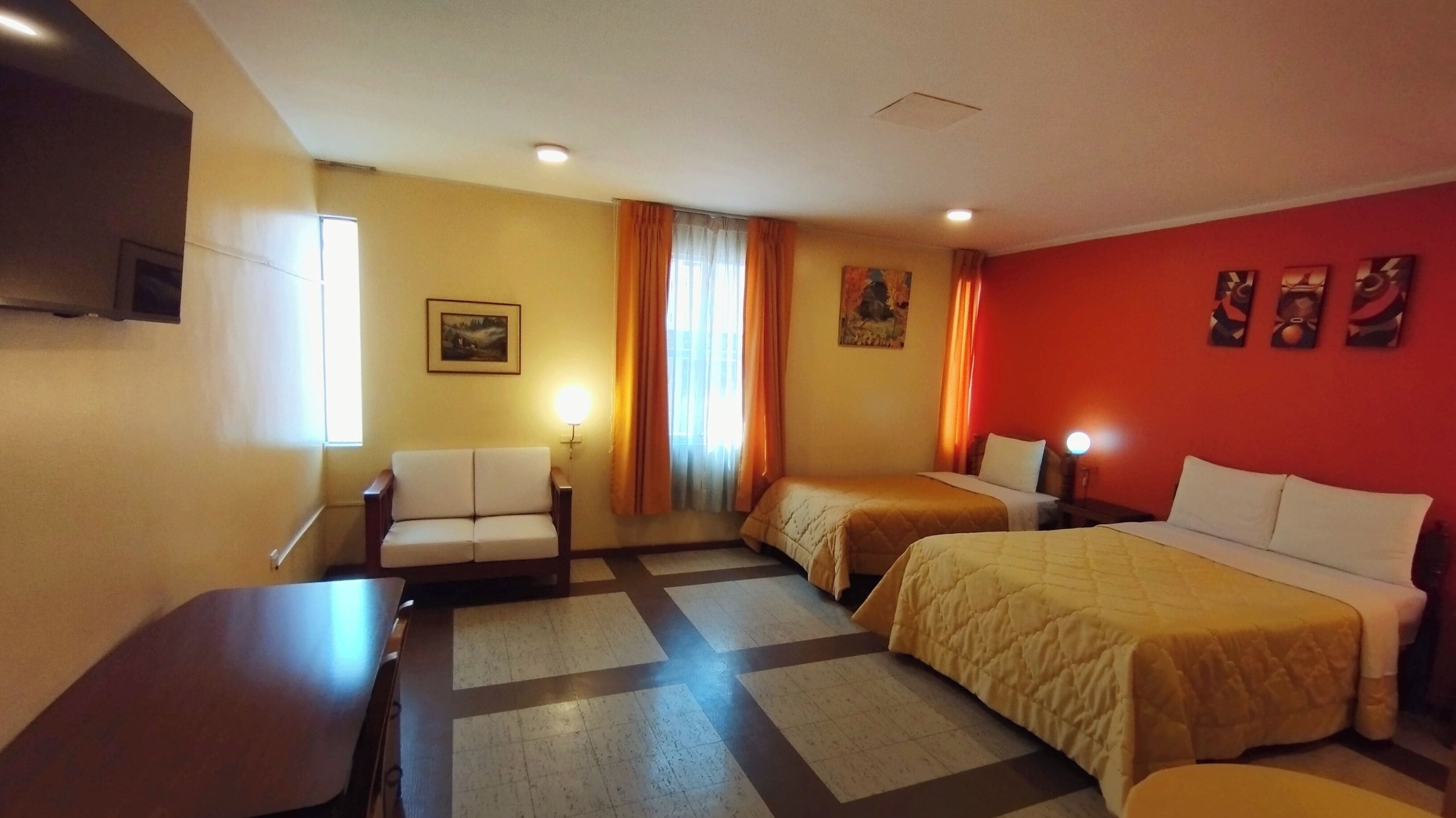 A hotel room with two beds, a sofa, a desk, and a television.