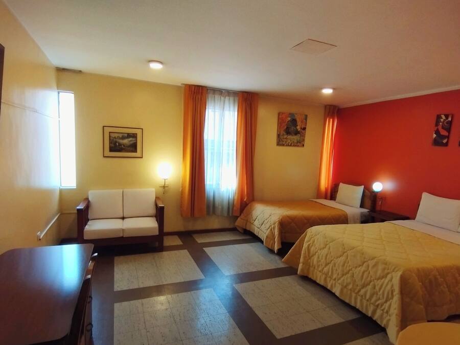 A hotel room with two beds, a sofa, a desk, and a television.