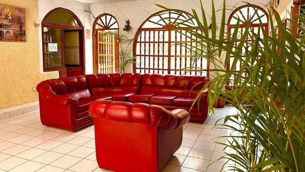Un hall con sofás de cuero rojo, ventanas amplias con marcos de madera y plantas en macetas.