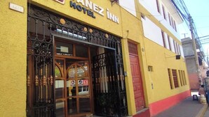 Entrada de un hotel con fachada amarilla, puerta roja y un letrero que indica que es un Hotel Yanez.