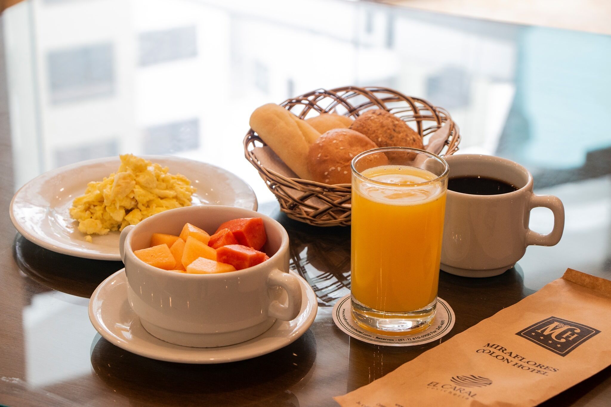 A breakfast setting with scrambled eggs, orange juice, and a basket of bread.