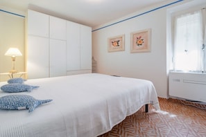 A bedroom with a bed, a wardrobe, a lamp, and two framed pictures on the wall.