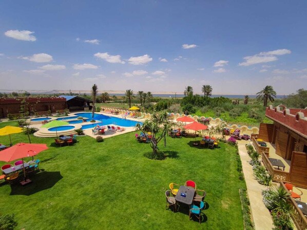 A pool area with multiple swimming pools, sun loungers, and umbrellas. - Tunis Pyramids Hotel (Yusuf as-Sidiq)