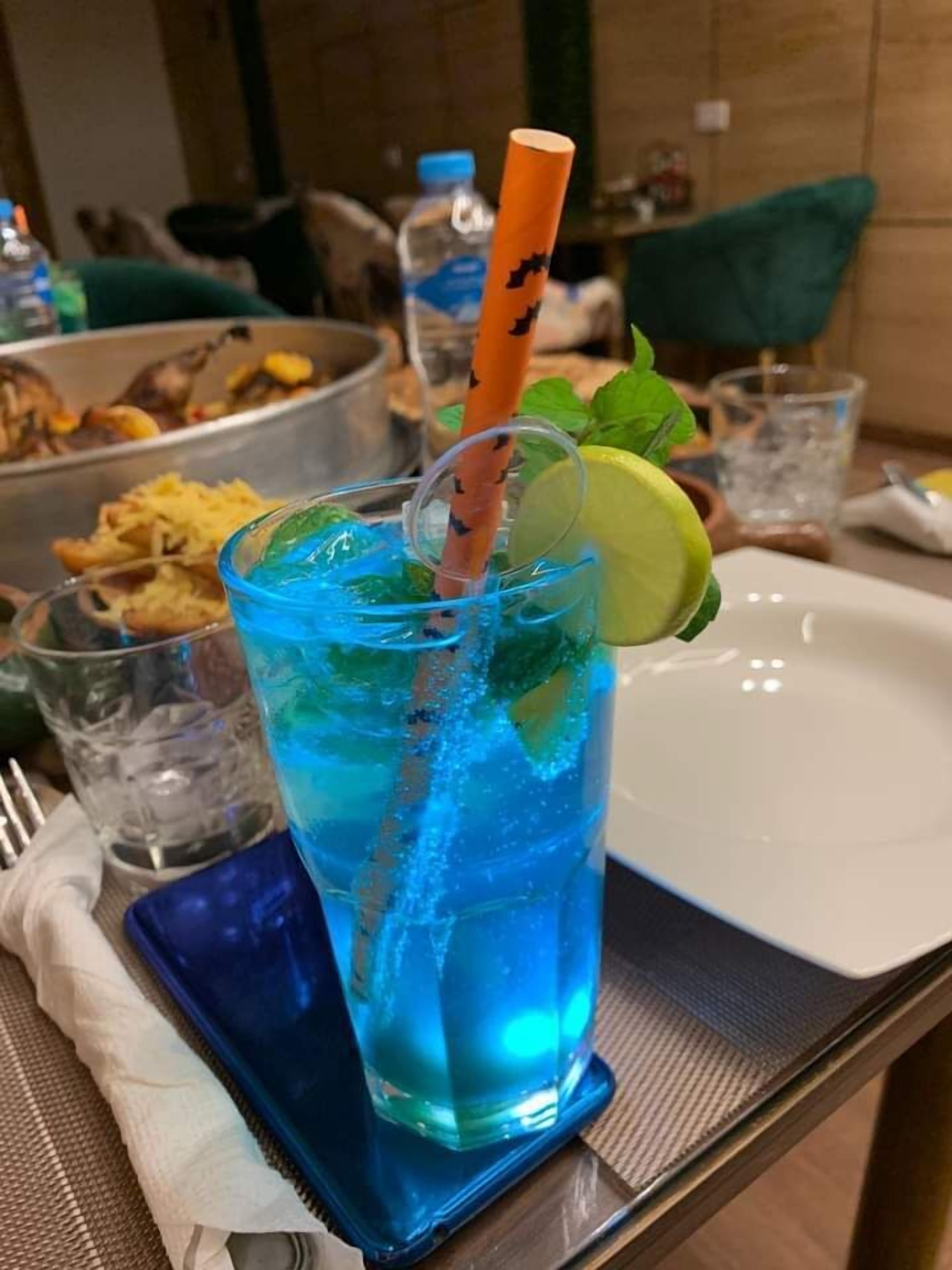 A glass of blue beverage with a straw and lime garnish, placed on a tray with a napkin and fork.