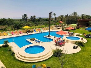 A large outdoor swimming pool with multiple sections, surrounded by colorful lounge chairs and umbrellas. - Tunis Pyramids Hotel (Yusuf as-Sidiq)