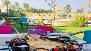 A dining table with a variety of dishes and a view of a pool and outdoor seating area. - Tunis Pyramids Hotel (Yusuf as-Sidiq)