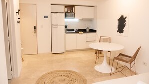 A modern kitchen with white cabinets, a white refrigerator, and a microwave. There is a dining table with two chairs and a woven rug on the floor. - Silencioso Studio en Palermo Hollywood (Buenos Aires)