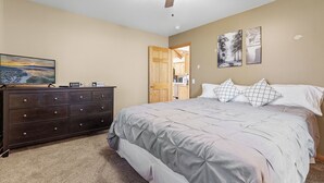 Een slaapkamer met een bed, een dressoir, een plafondventilator en kunstwerken aan de muur.