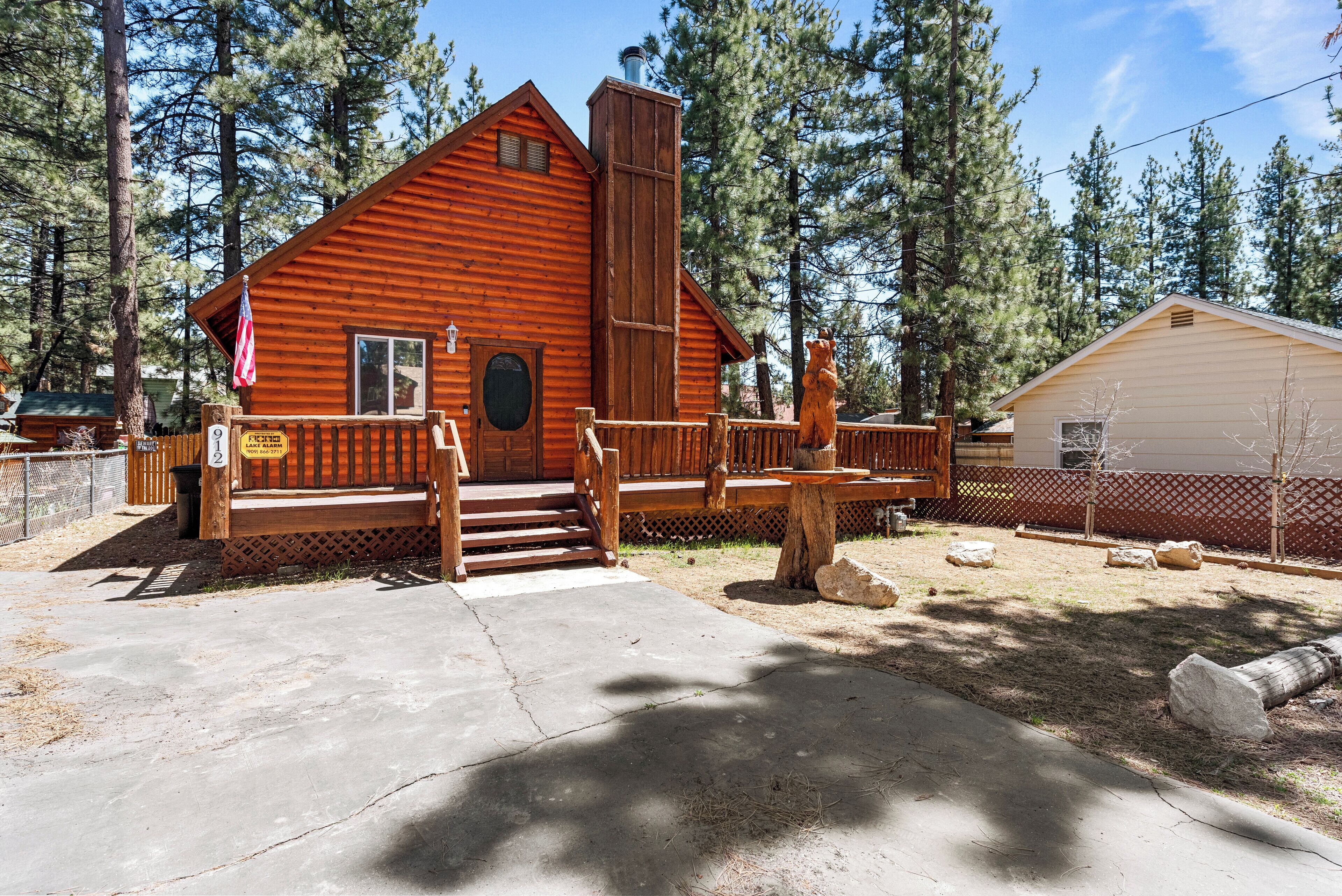 A rustic cabin with a wooden deck, a chimney, and a fenced yard.