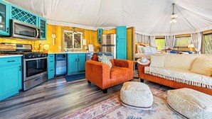 A tented accommodation with a kitchen, orange sofa, and a beige sofa.