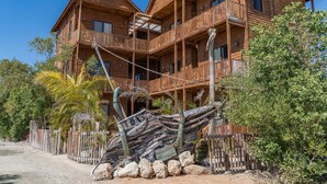 A wooden multi-story building with balconies, surrounded by tropical vegetation and a large shipwreck. - Krak-Inn Holbox Self Check In (Isla Holbox)