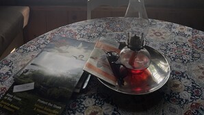 Une table recouverte d’une nappe à motifs, un vase en verre, un plateau en métal et des brochures.