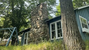 Une cheminée en pierre, un grand arbre et un bâtiment doté de fenêtres.