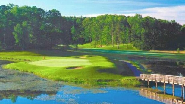 Un parcours de golf avec un plan d’eau, un pont en bois et une zone boisée.