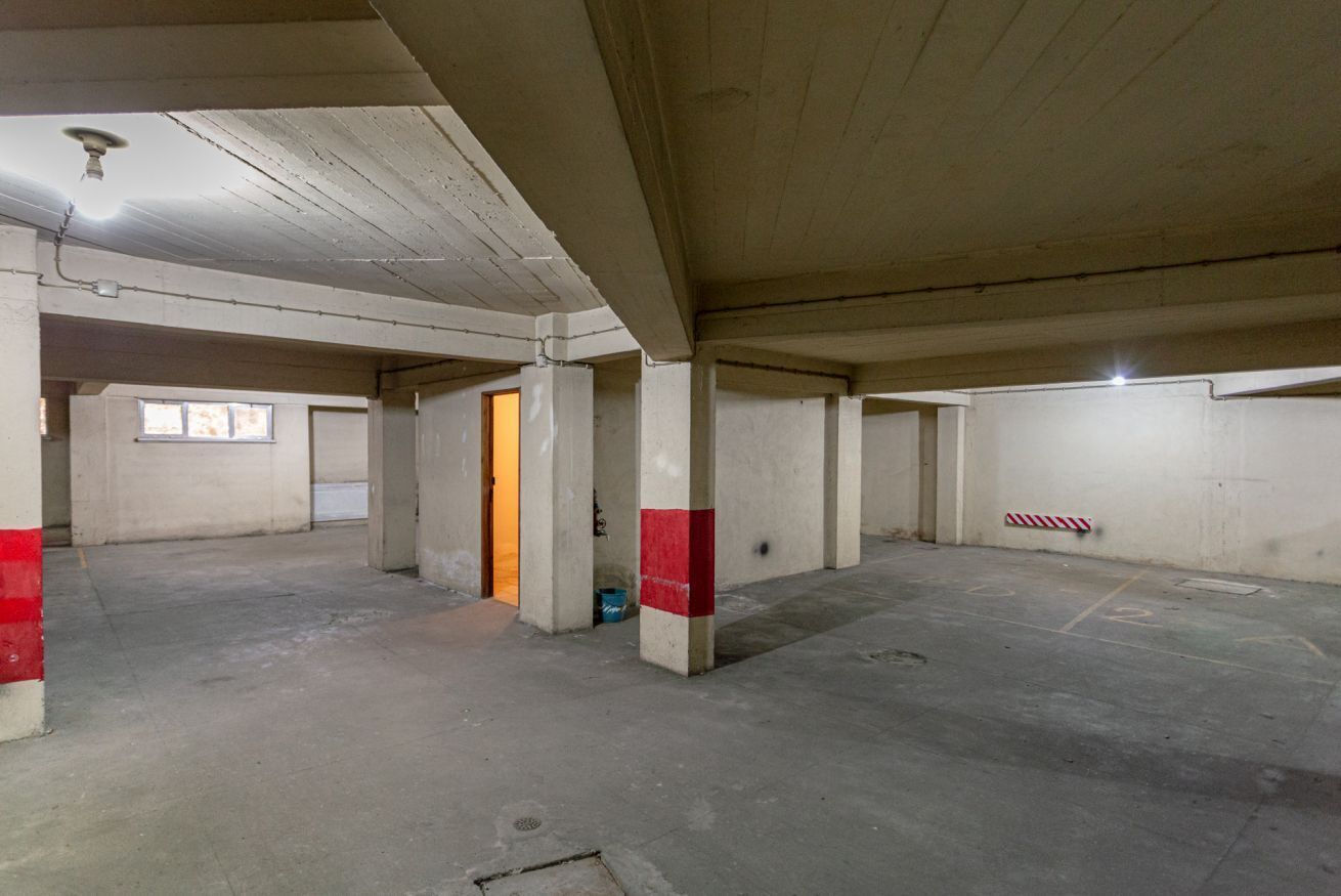 An empty parking garage with concrete pillars, a door, and a striped barrier.