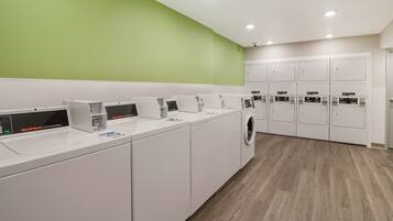 A modern laundry facility with multiple washing machines and dryers, a green wall, and a wooden floor.