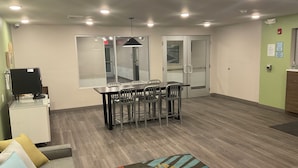 Un espace de bureau moderne comprenant une table de conférence, des chaises, un petit coin cuisine et un tapis à motifs.