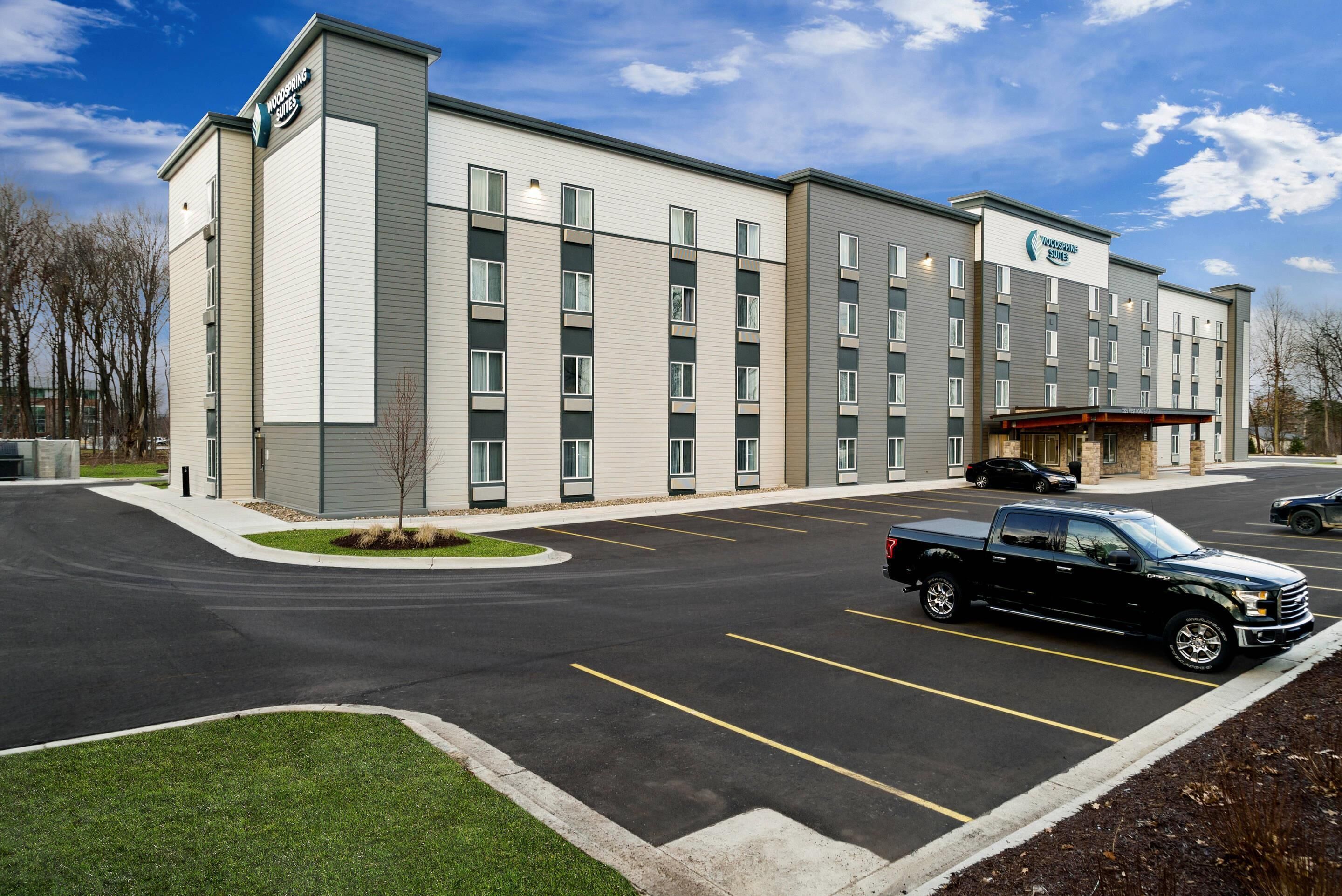A modern hotel with a parking lot, a covered entrance, and a well-maintained lawn.