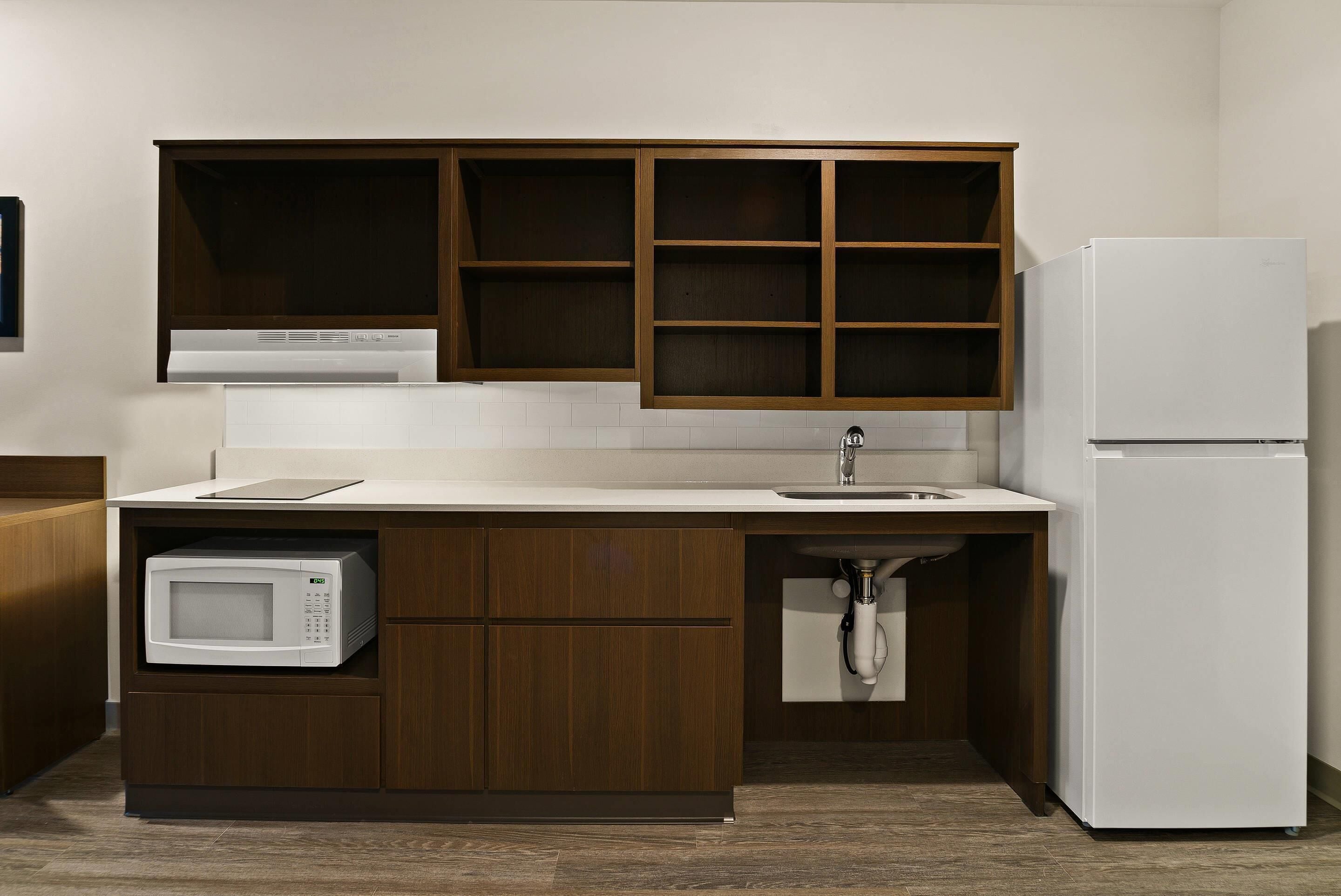 A compact kitchen with wooden cabinets, a built-in microwave, a sink, and a white refrigerator.