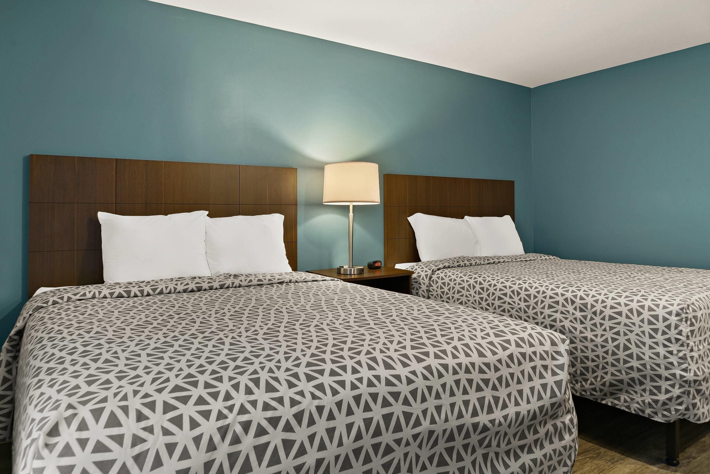 Habitación de hotel con dos camas, cada una con una colcha de estampado geométrico, un cabecero de madera y una mesita de noche con lámpara.