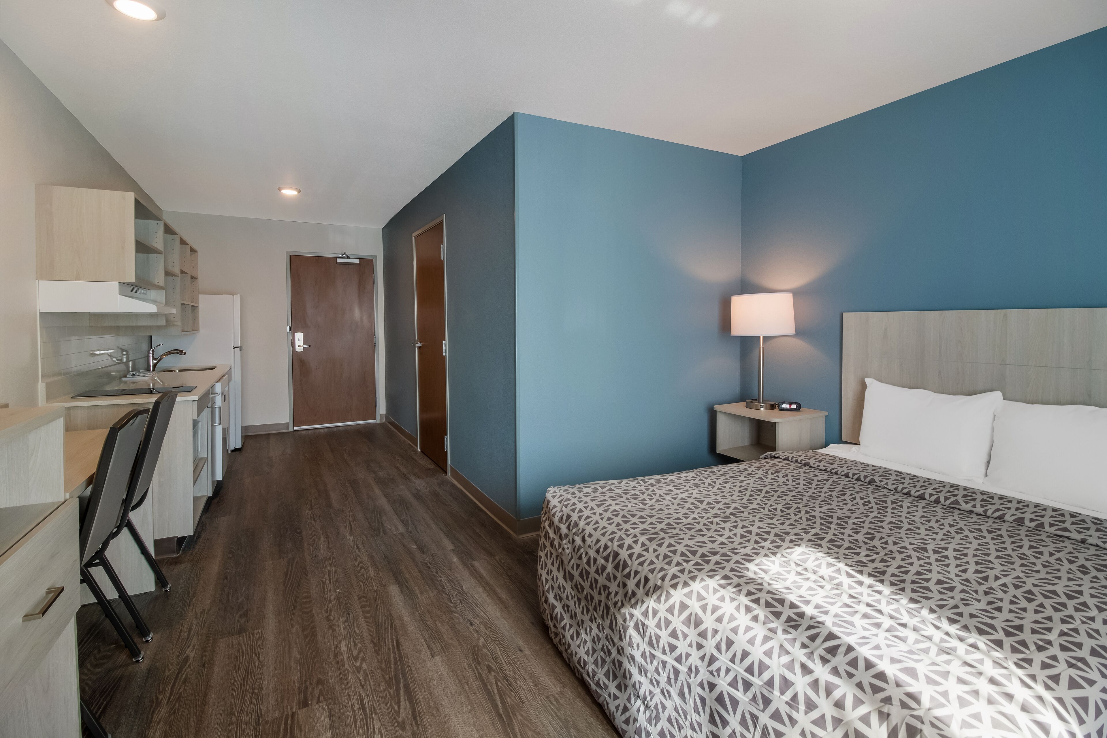 A hotel room with a bed, a desk, and a kitchenette.
