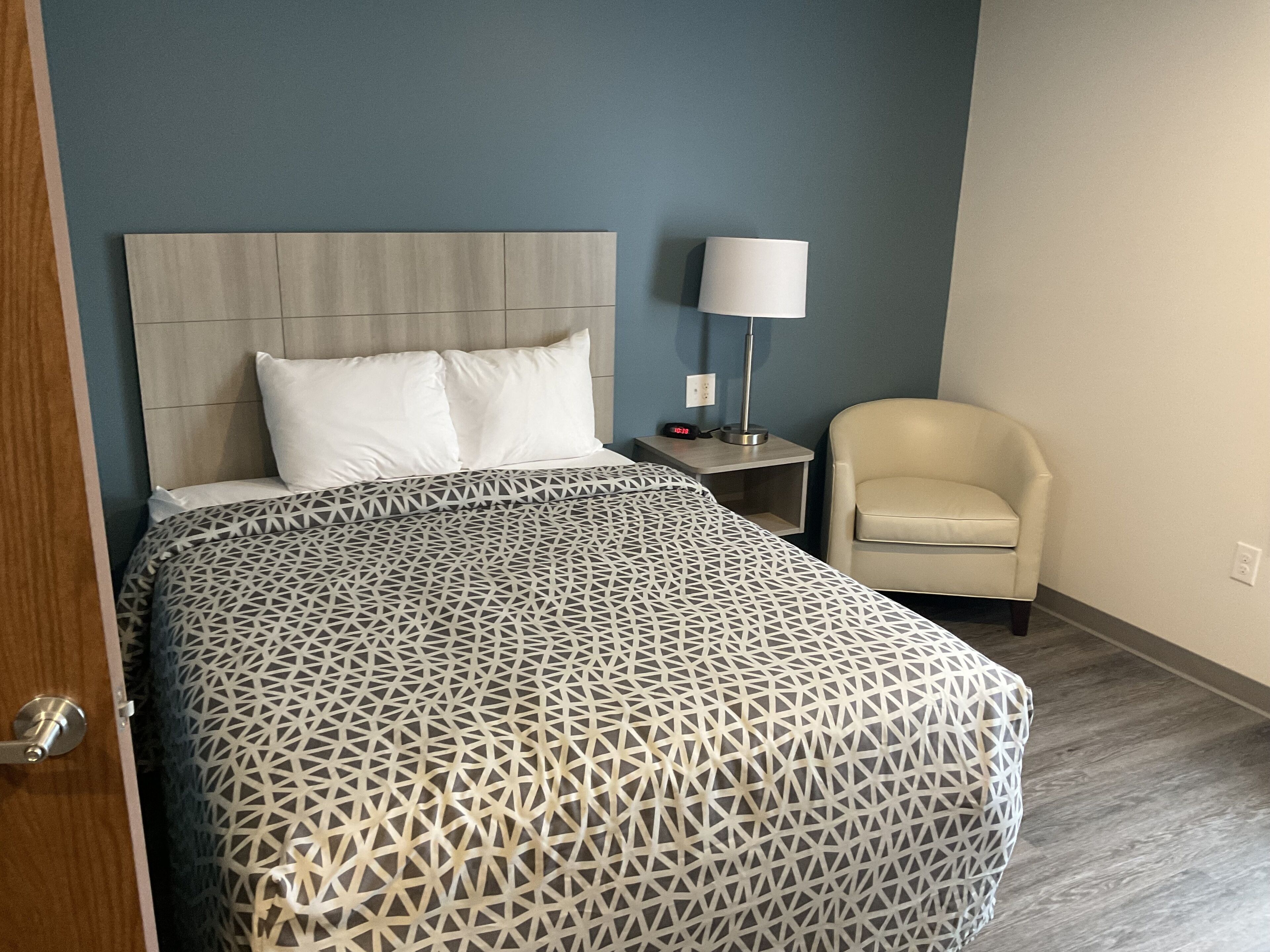 A hotel room with a bed, a nightstand, a lamp, and a chair.