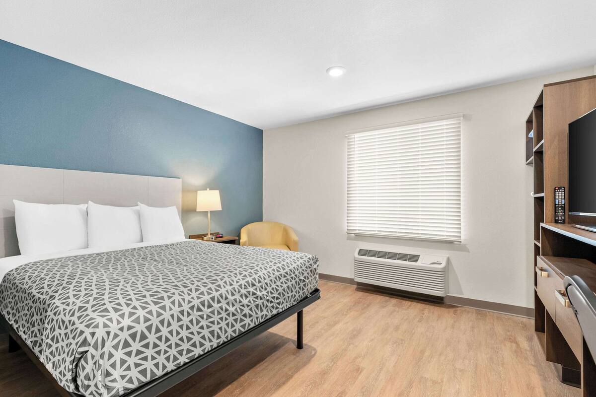 A hotel room with a bed, a desk, a chair, a TV, and a window with blinds.