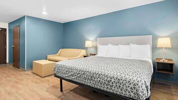 Una habitación de hotel con cama, una silla, dos mesitas de noche con lámparas y una puerta.