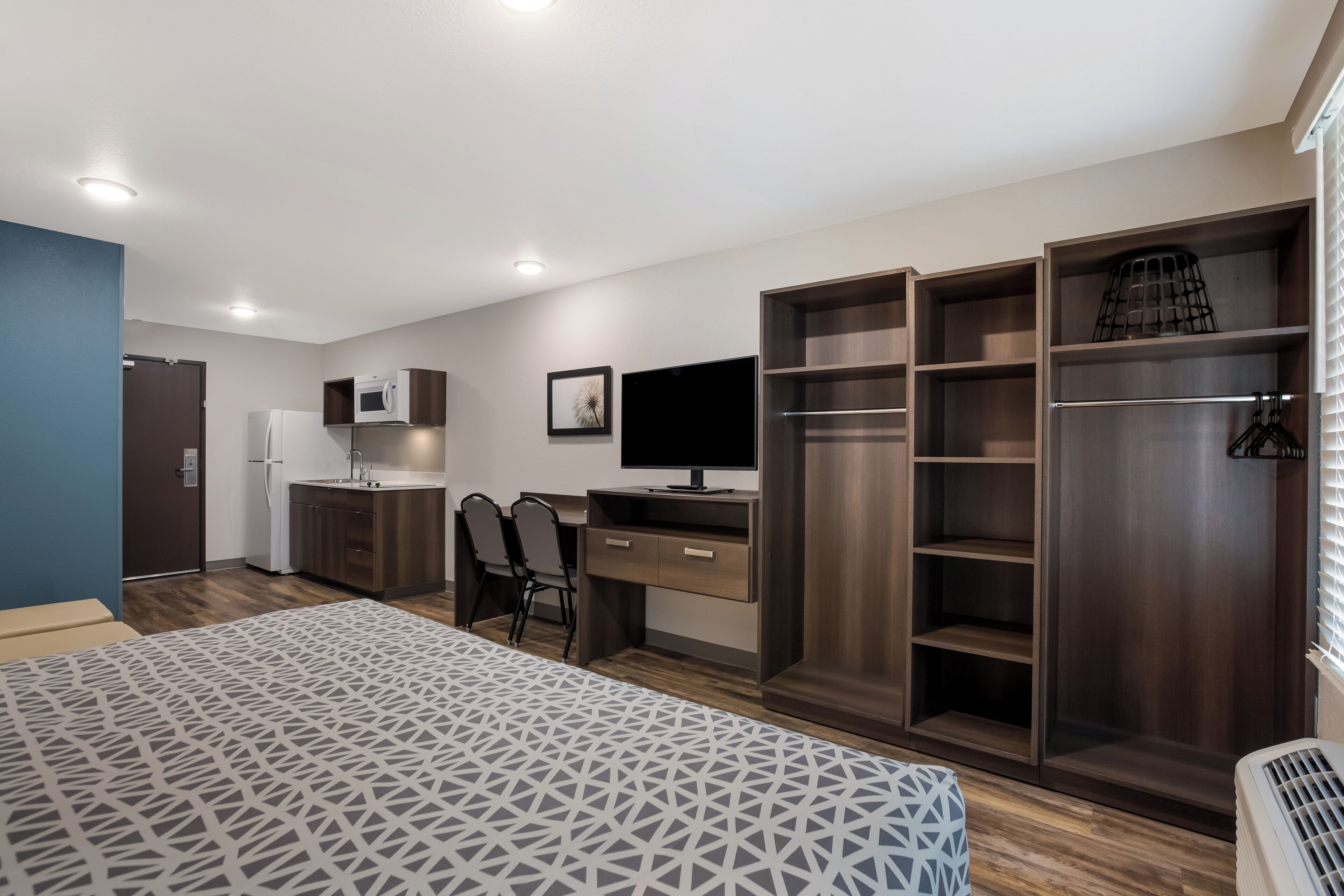 A modern bedroom with a bed, a desk, a TV, and built-in wardrobes.