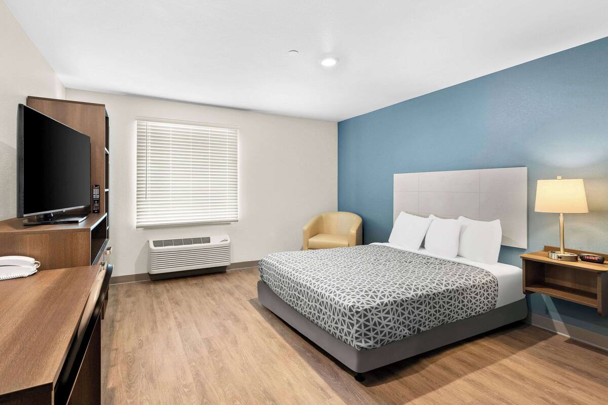 A hotel room with a bed, a TV, a chair, a desk, and a lamp.