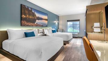 Quarto de hotel com duas camas, uma escrivaninha, uma cadeira, uma janela grande e um quadro na parede.