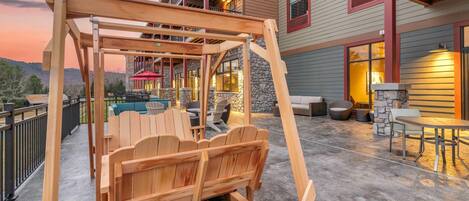 A wooden swing set and seating area on a concrete patio with a view of a building with balconies and windows.