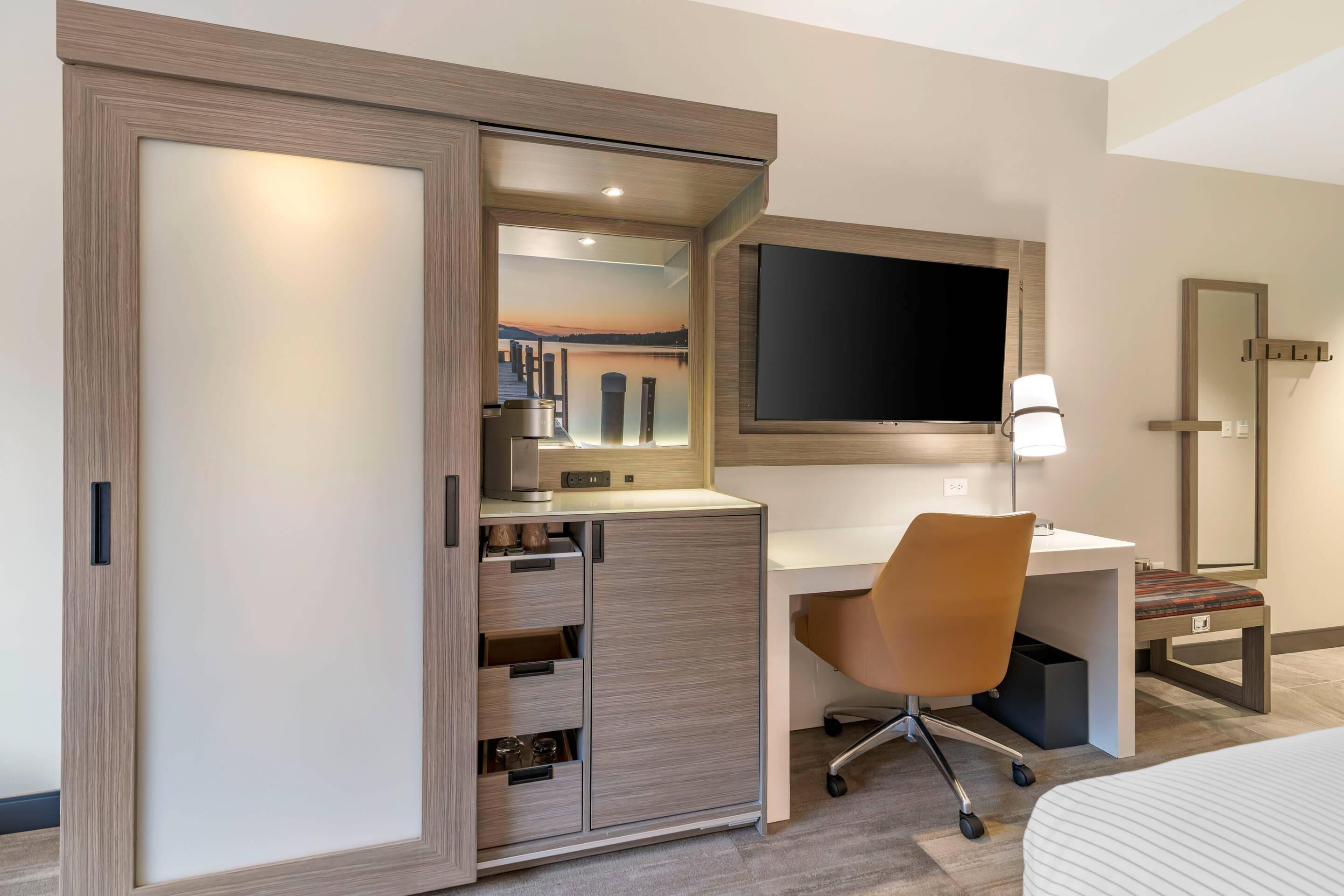 A hotel room with a desk, chair, bed, and a sliding wardrobe with a view of a lake.