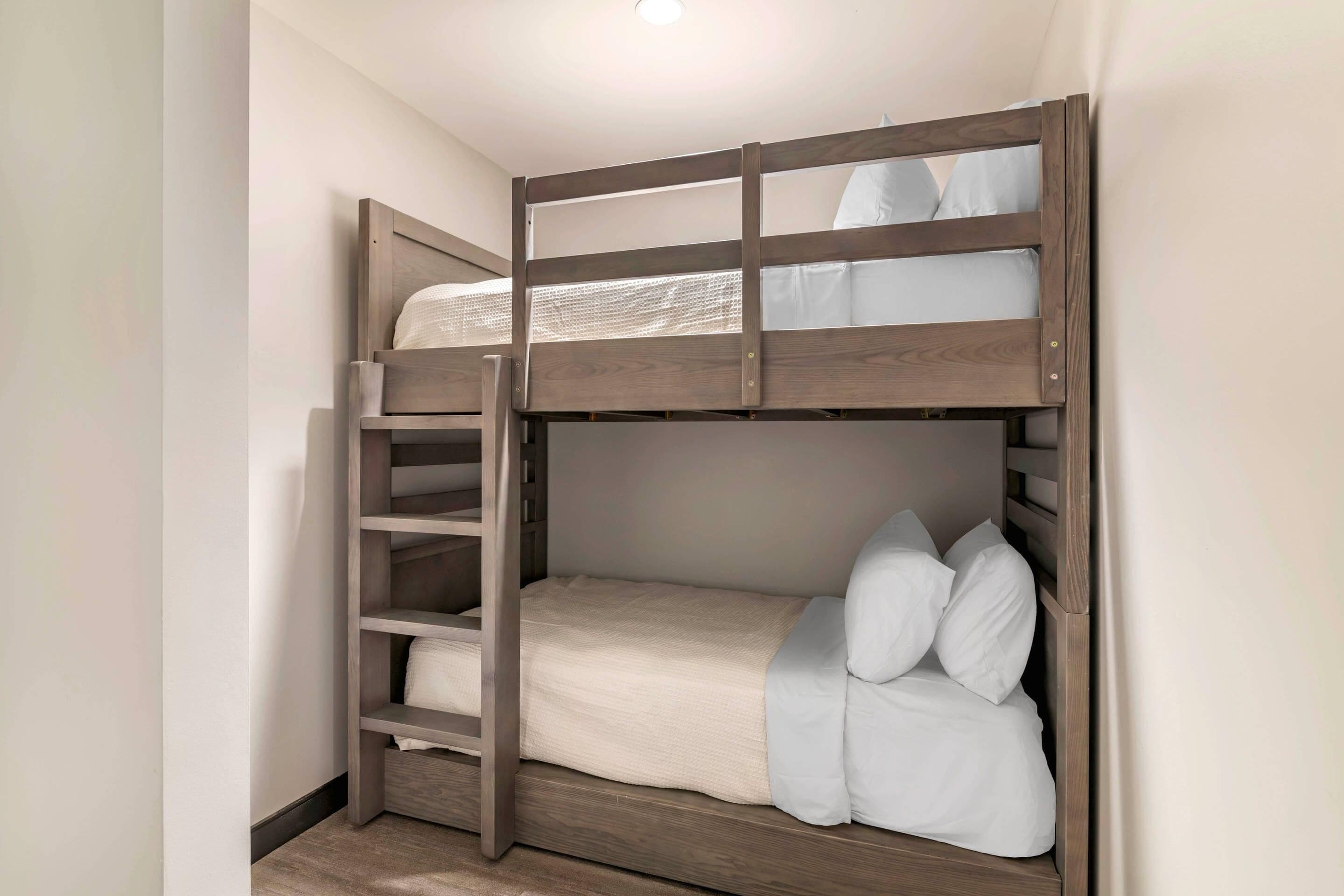 Un lit superposé avec une échelle, du linge de lit blanc et une structure en bois.