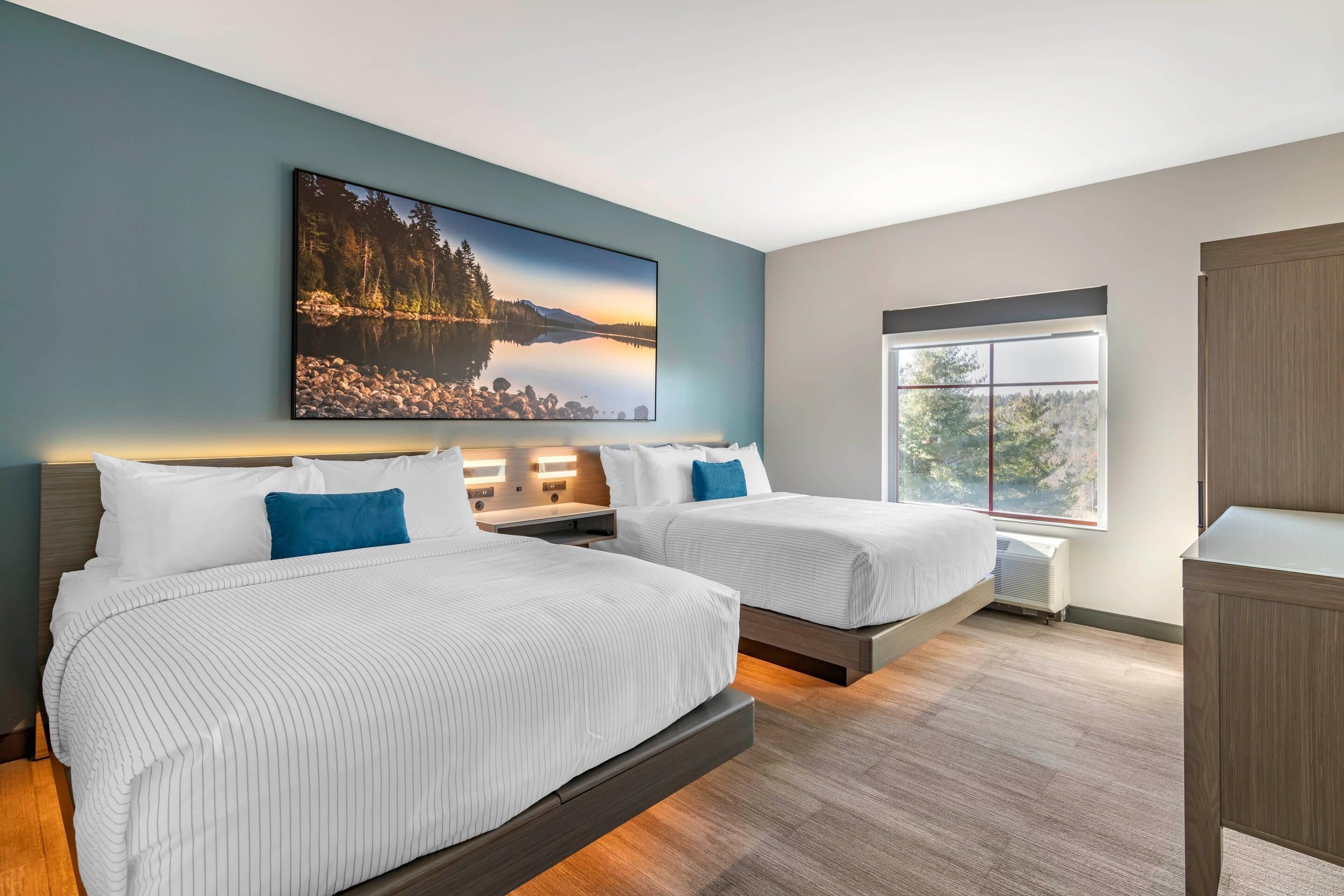 A hotel room with two beds, a large window, and a painting on the wall.