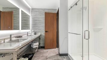 A modern bathroom with a double sink vanity, a glass shower enclosure, and a marble-patterned wall.
