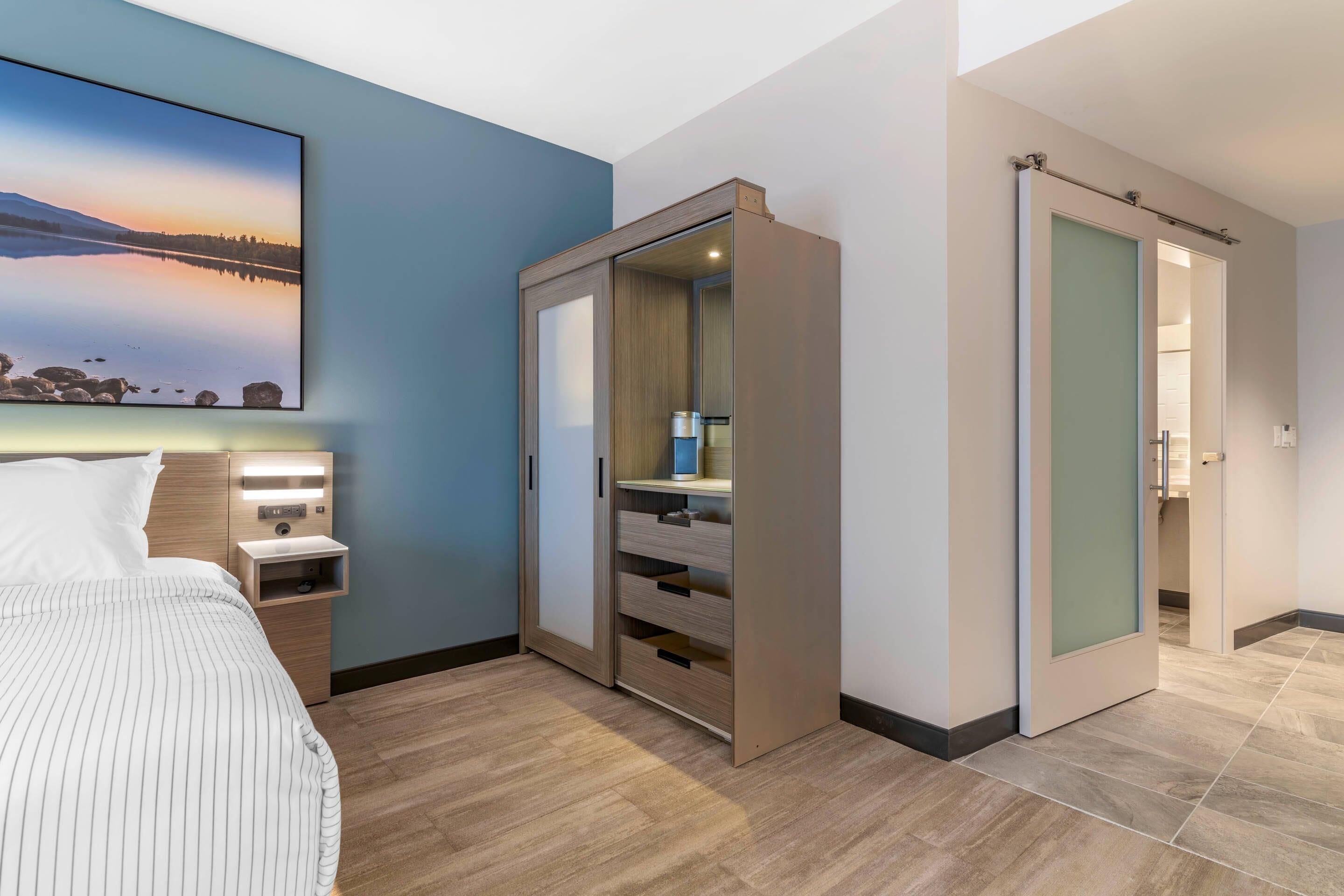 Una habitación de hotel moderna con cama, mesita de noche, un espejo grande y un armario con puerta corredera.