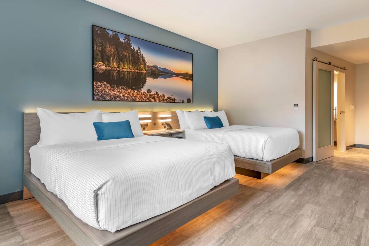 A hotel room with two beds, a large framed picture of a lake, and a wooden floor.