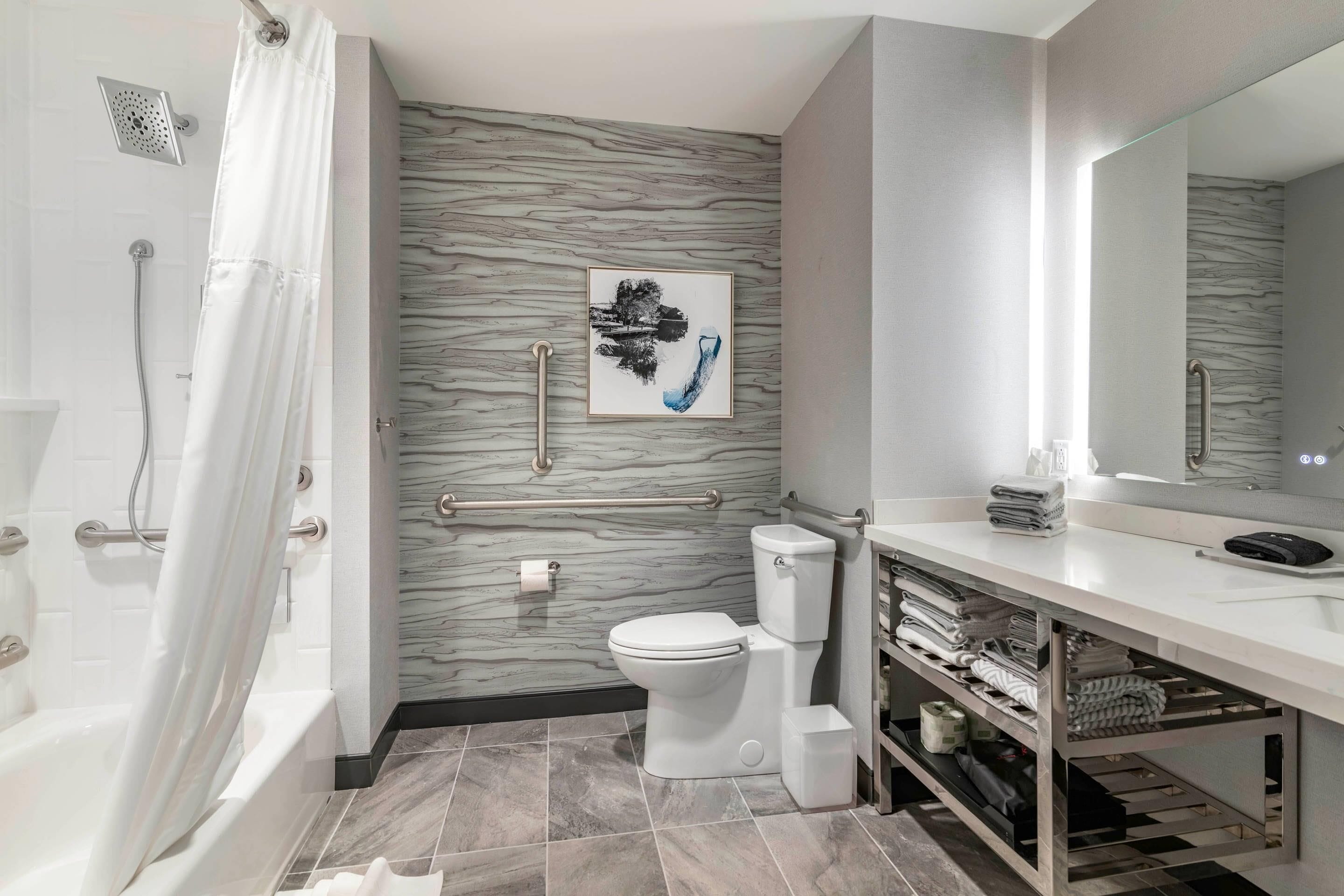 A modern bathroom with a marble wall, a toilet, a bathtub, and a vanity with a mirror.